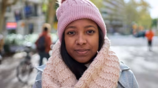 Woman in pink knit hat and beige scarf on a city street in autumn