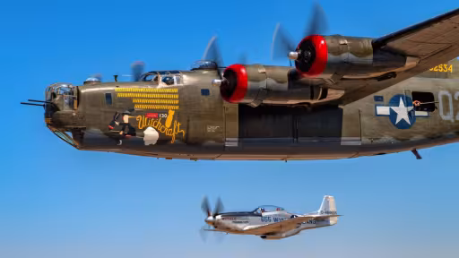 Two vintage military planes flying in formation against a clear blue sky